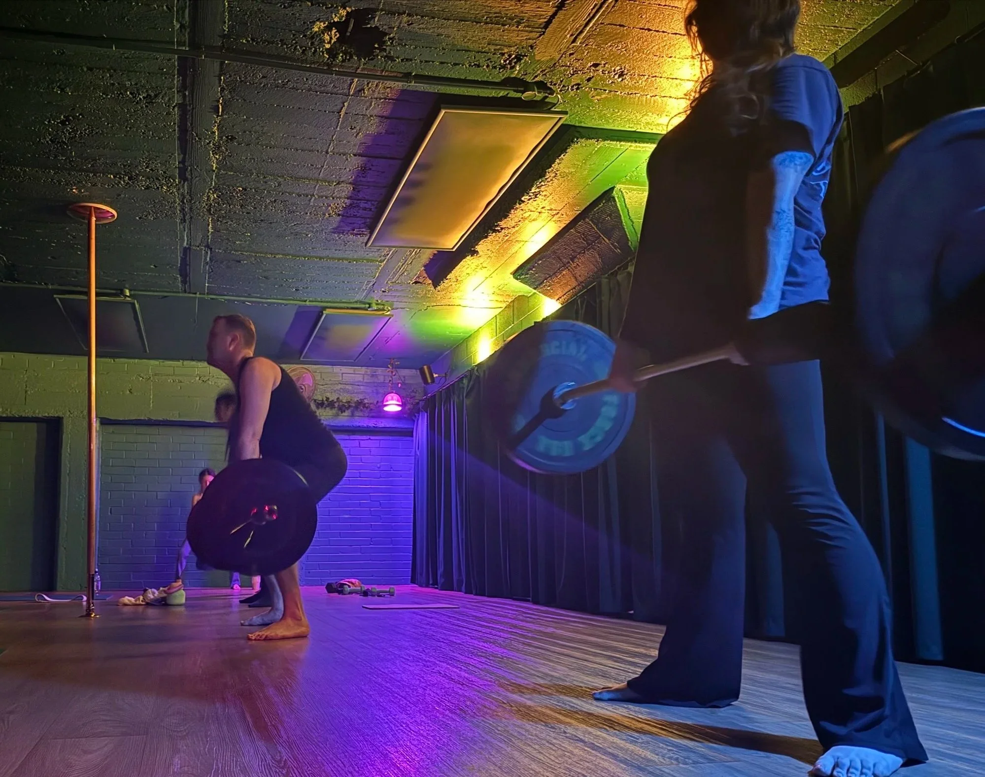 People doing yoga or stretching exercises in a dimly lit studio with colorful ambient lighting.