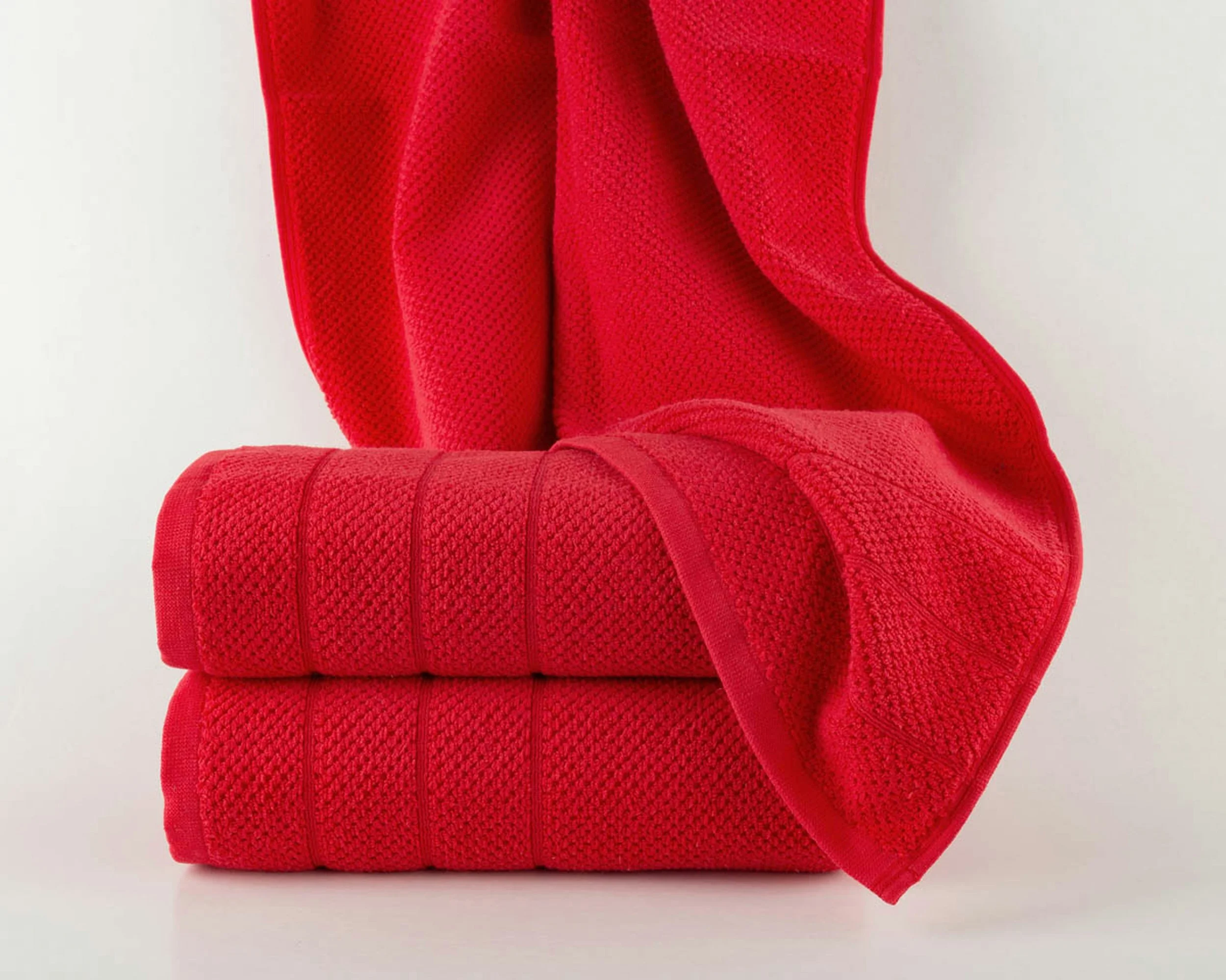A close-up of a red woven fabric with a textured pattern, folded and draped against a white background.
