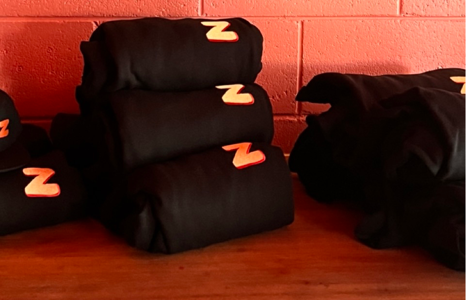 Stacks of black clothing with a red and yellow 'Z' logo, placed on a wooden surface against a brick wall.