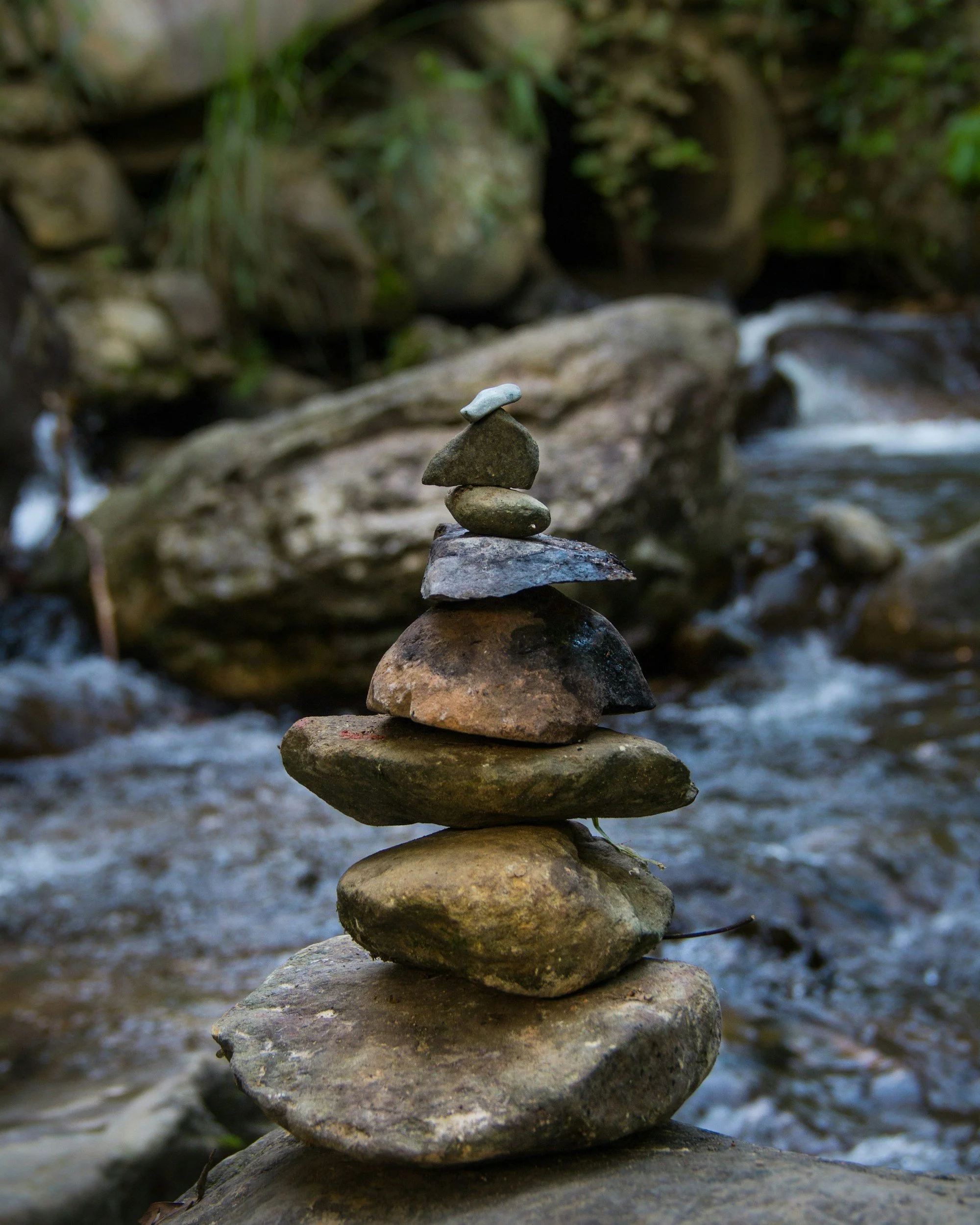 Balanced stone stack by a flowing stream, representing stability and calm focus during the healing process.