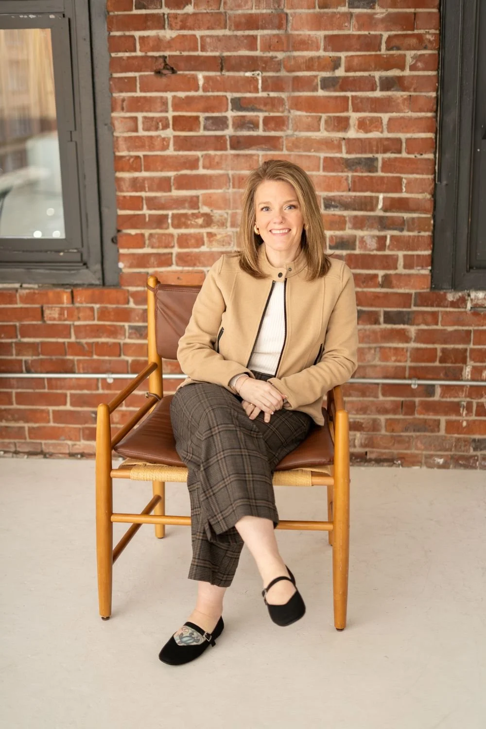 Jennifer Weinmann sitting in an office chair, linking to the About Me page.