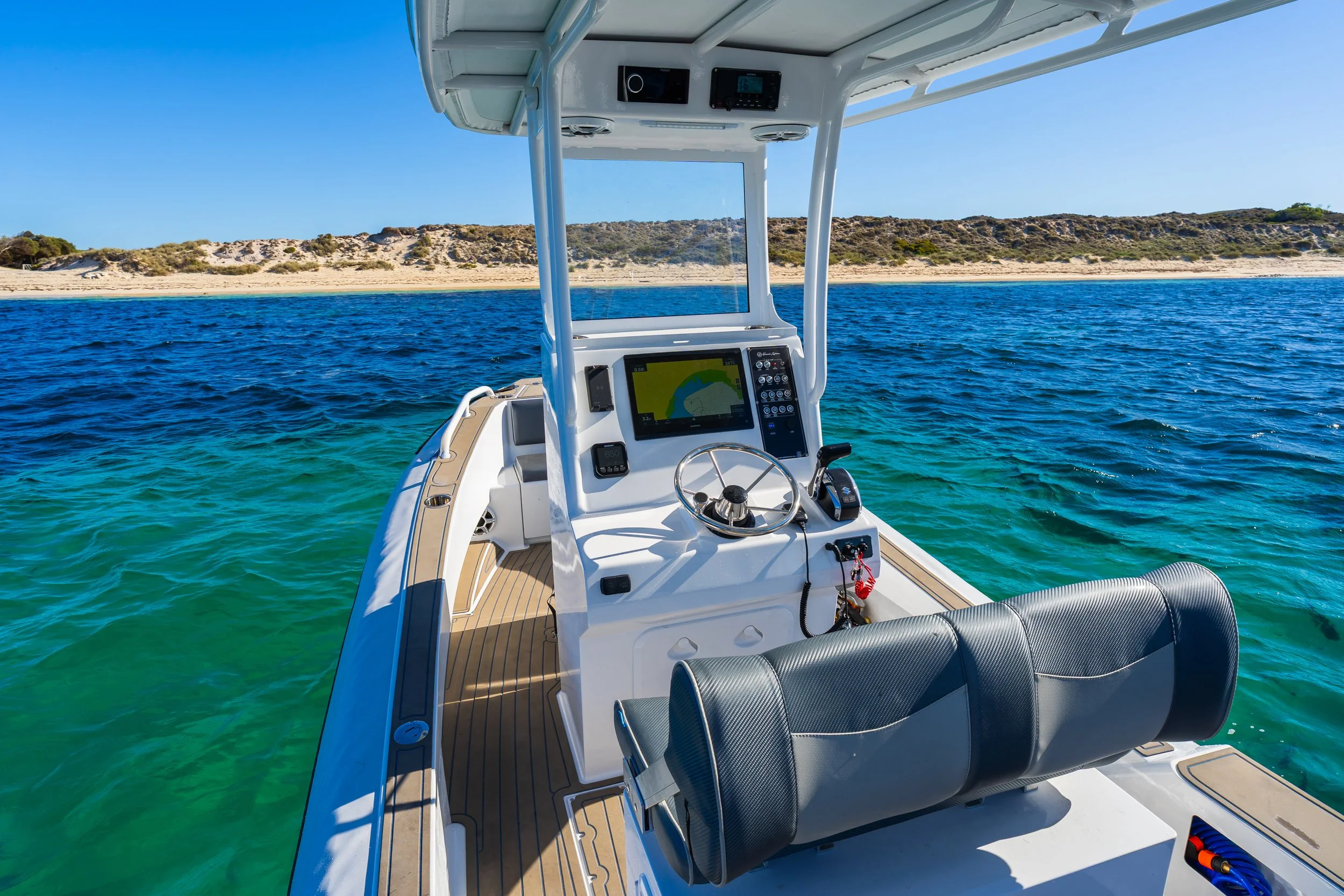 View from a boat looking towards a sandy beach with hills on a clear, sunny day.
