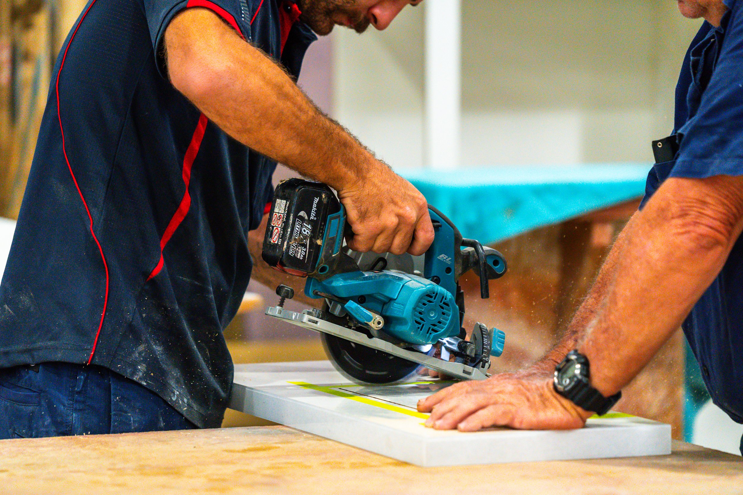 Workers using a power saw to cut through a piece of wood in a workshop.