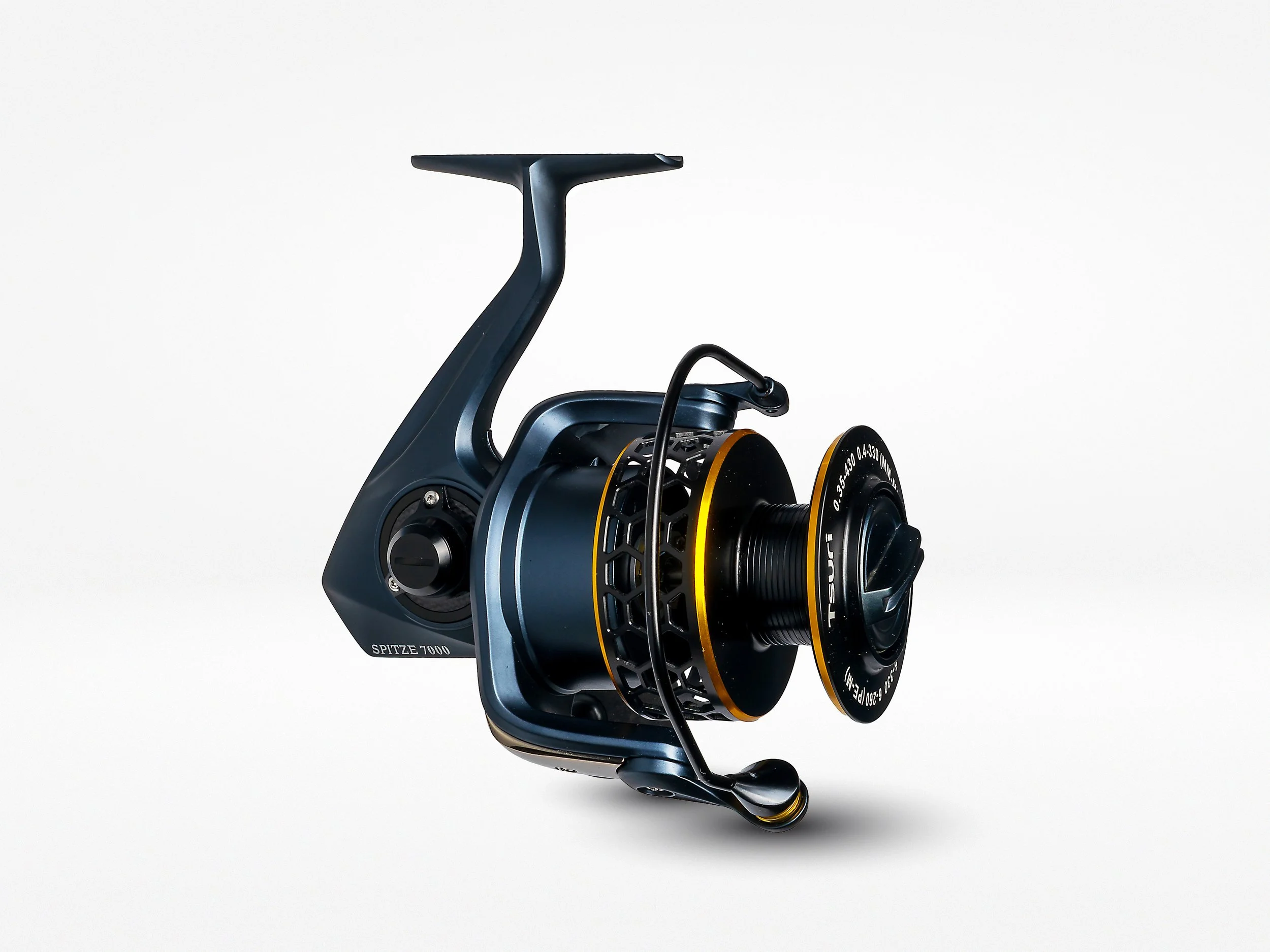Close-up of a modern fishing reel with a metallic blue finish, black accents, and gold detailing, labeled 'SPITZE 7000', against a plain white background.