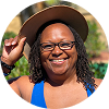 Smiling Black woman  with sisterlocks wearing glasses and a blue shirt outdoors