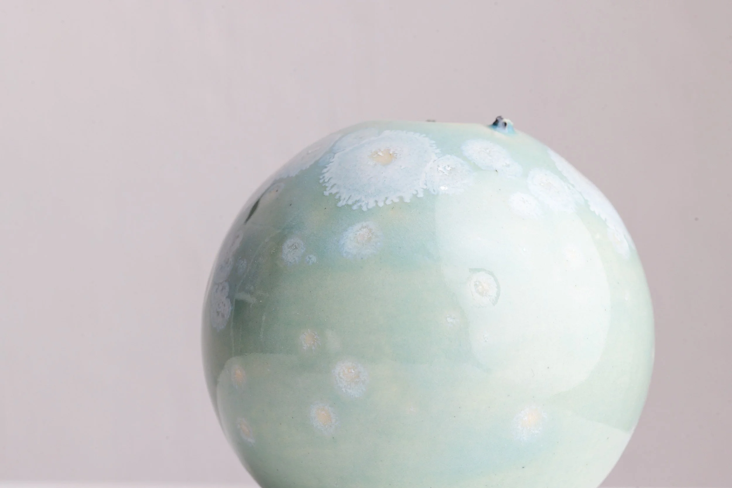 Close-up of a ceramic or glass object with a pastel green surface and white floral patterns, possibly a decorative piece or vase, against a plain gray background.