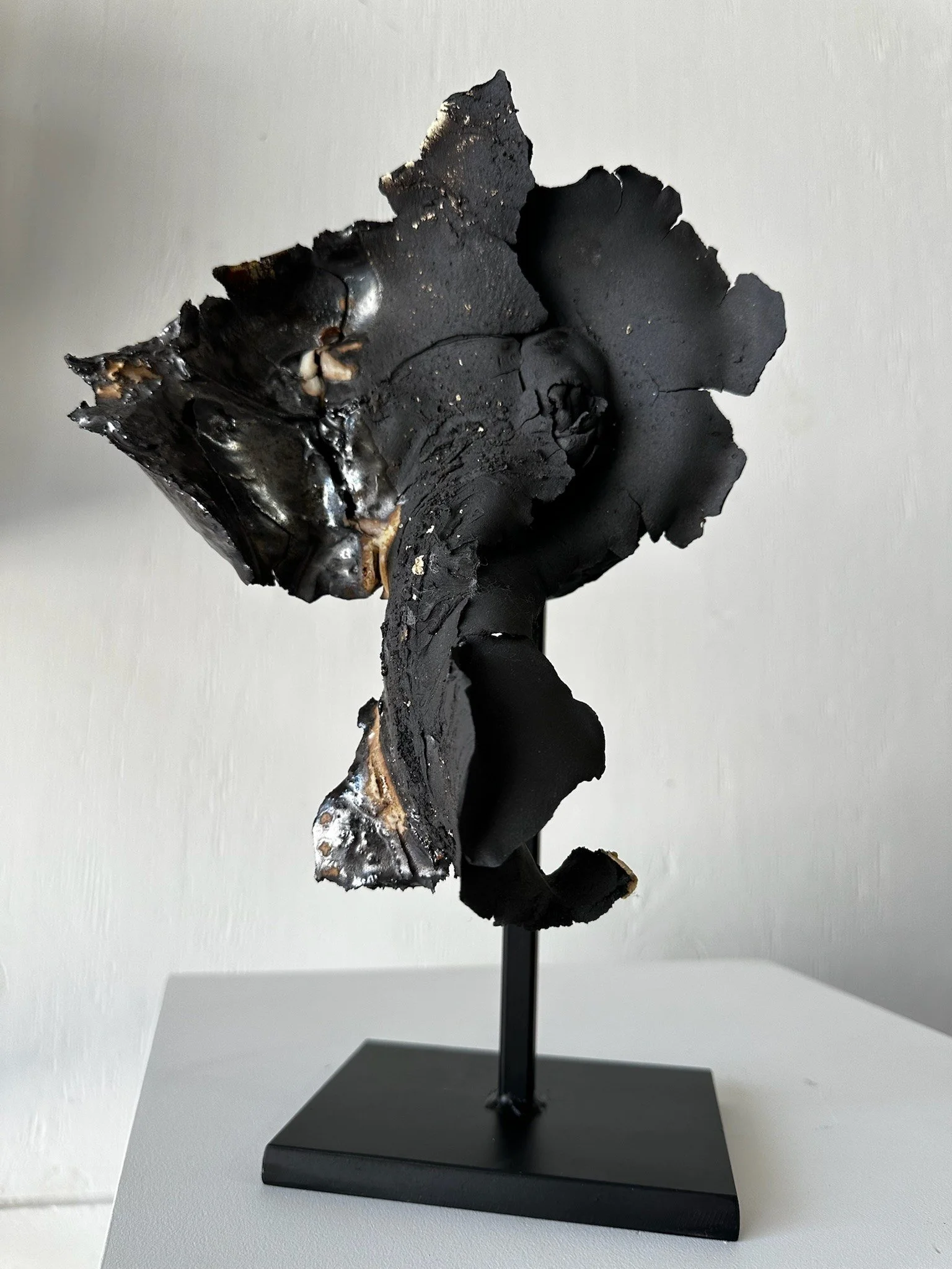 Sculpture of a black dog with a shiny surface on a black stand, set against a plain light background.