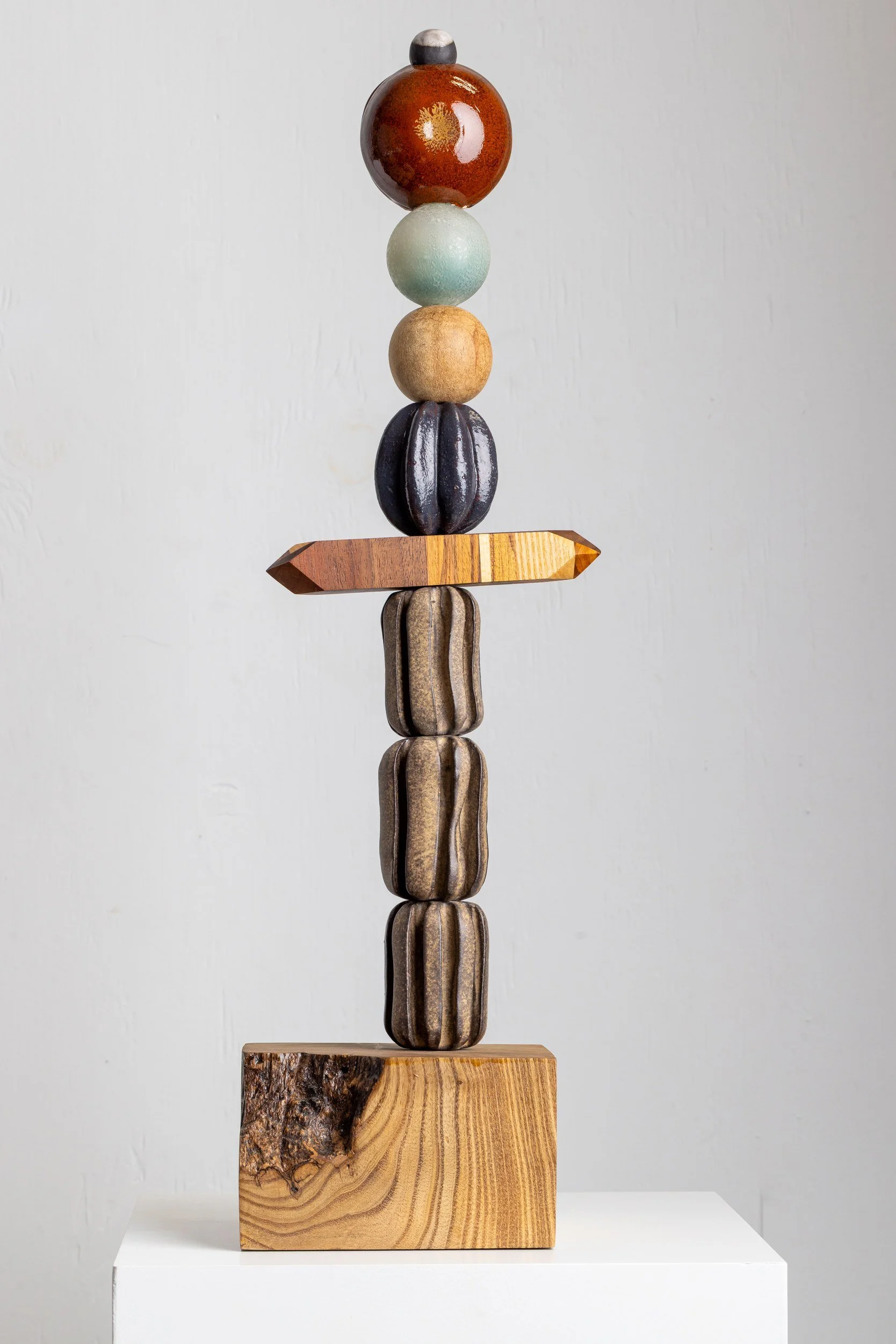 A balanced sculpture made of various carved and painted wooden shapes stacked vertically on a wooden base.
