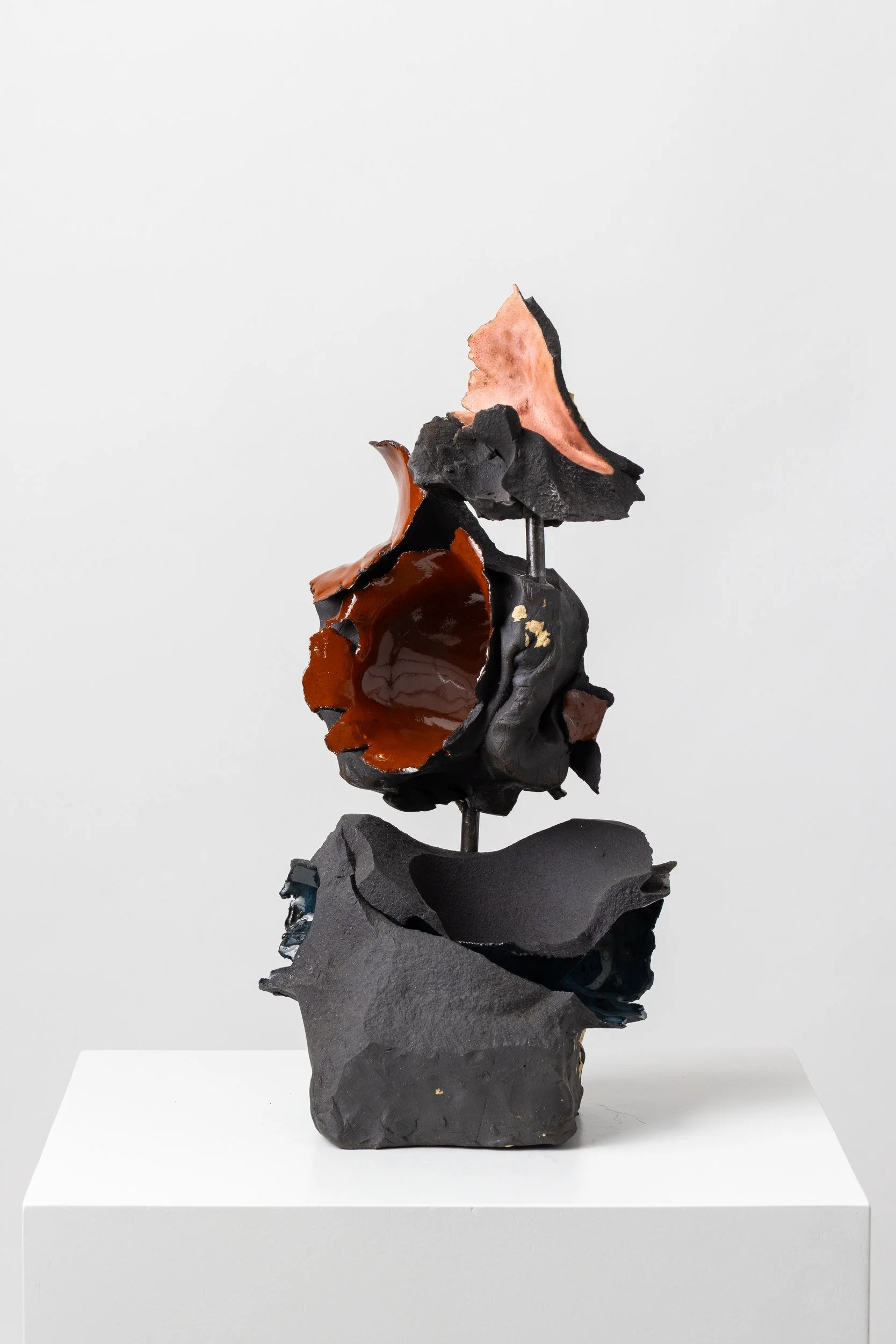 An abstract sculpture composed of irregular black, brown, and pinkish materials stacked vertically on a white base.