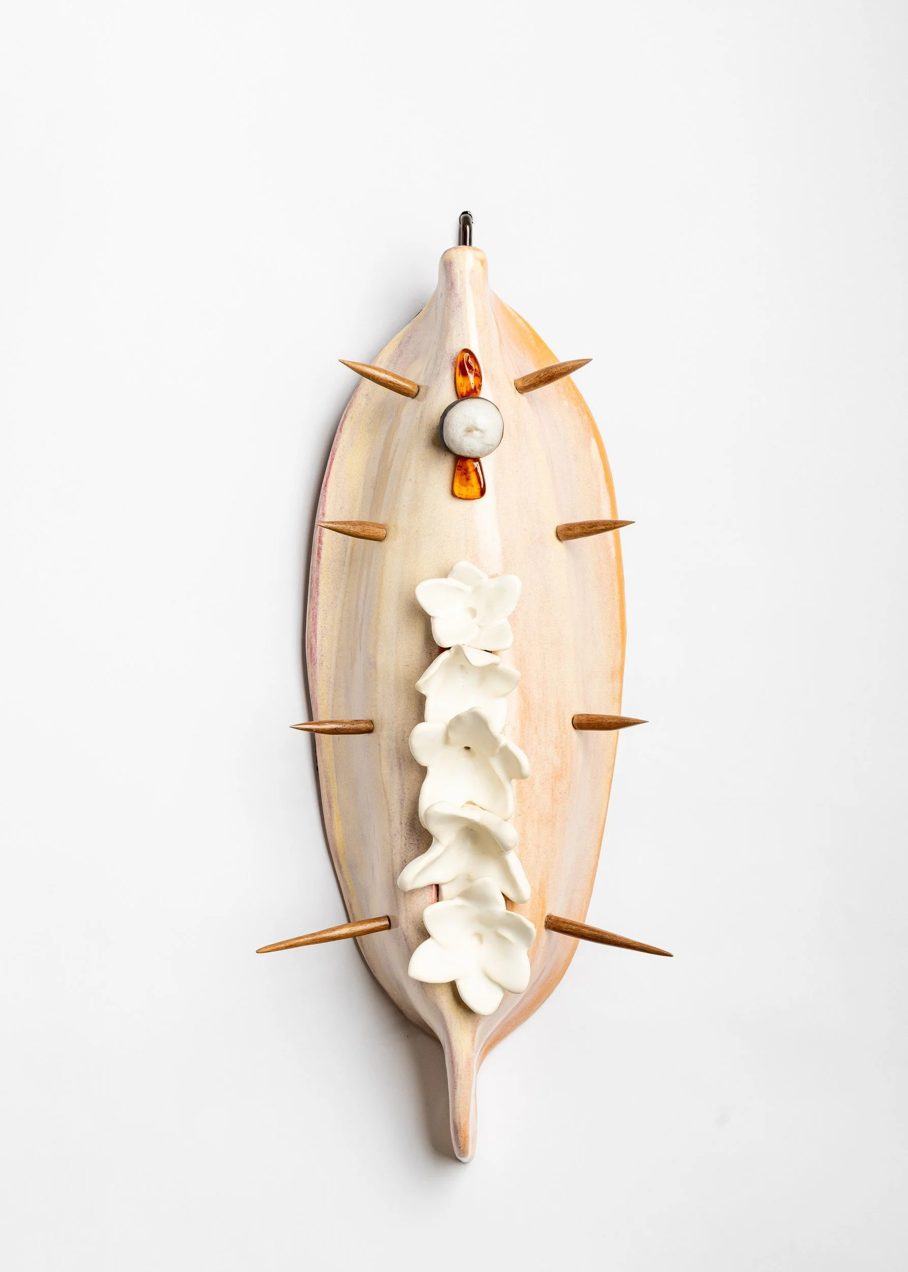 Decorative wall art resembling a wild boar's face, made from a seashell with wooden spikes as tusks, a white stone nose, and shells for eyes and decoration.