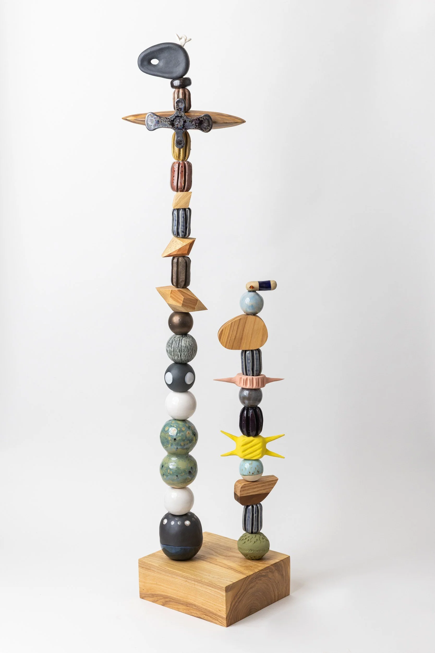 Sculpture made of various colorful ceramic and wood objects balanced on two vertical poles mounted on a wooden base.
