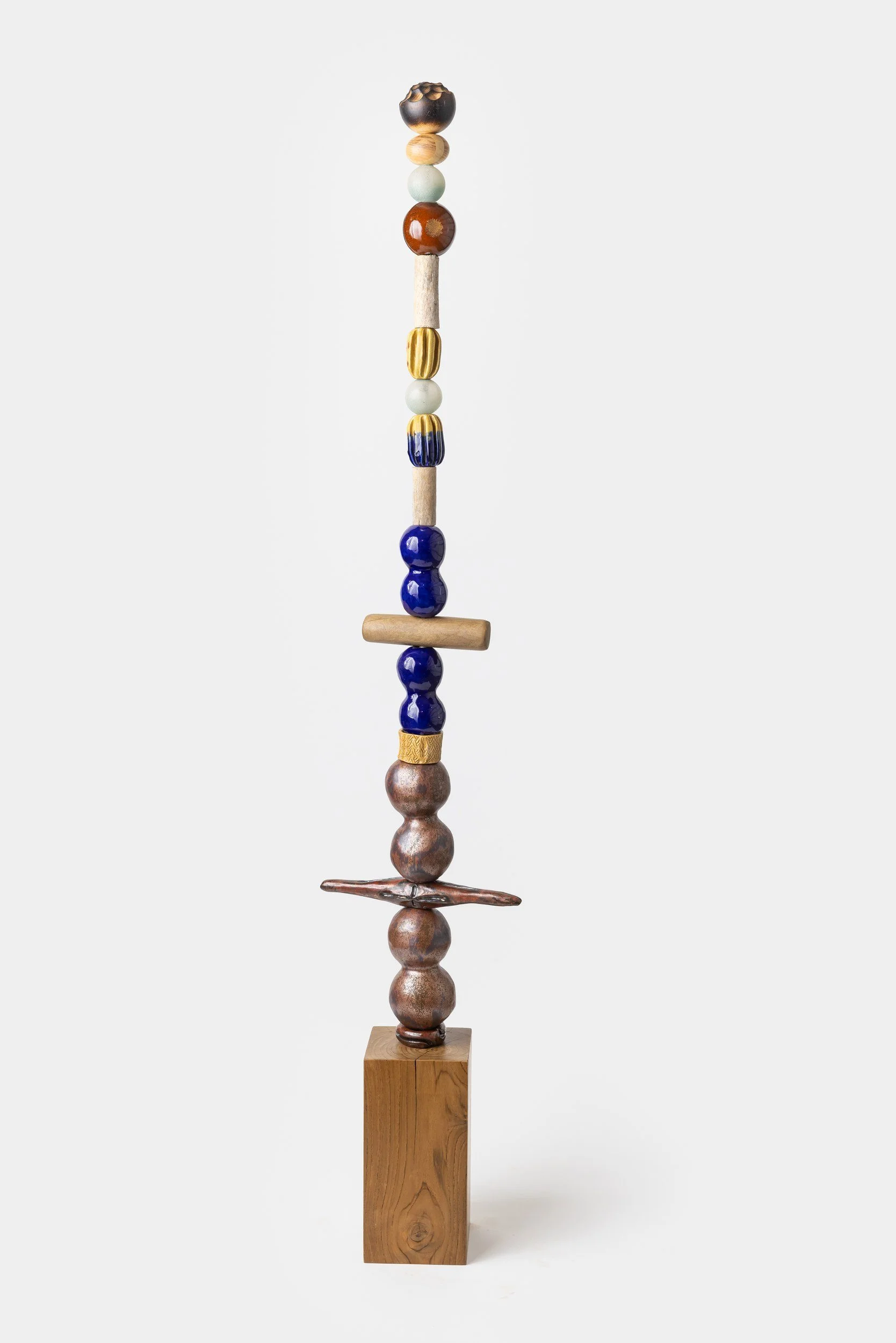 An abstract sculpture made of various colorful beads, wooden shapes, and metal pieces, stacked vertically on a tall wooden base.