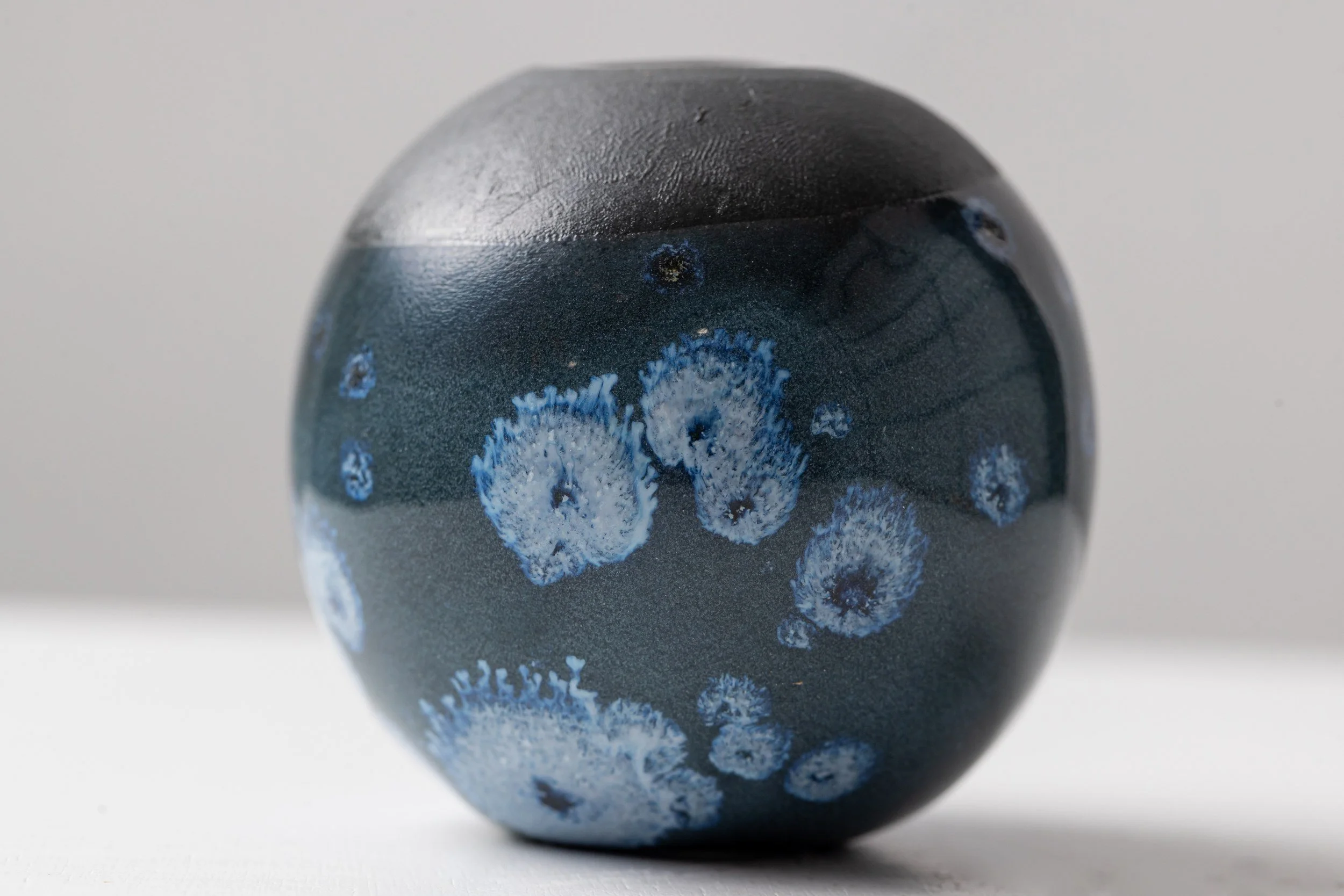Close-up of a black spherical object with blue floral patterns, reflecting a white background.