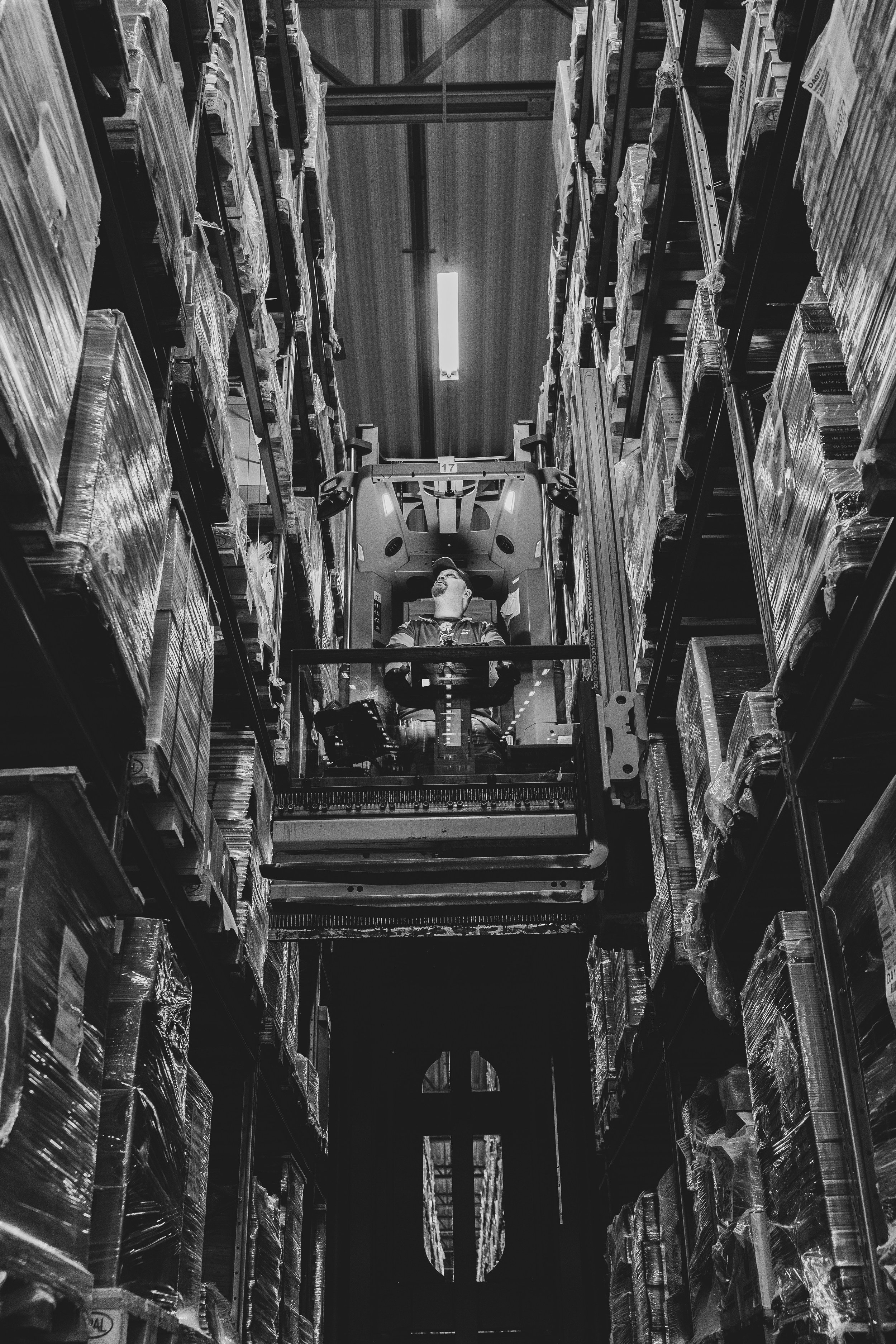 A person operating a forklift in a warehouse aisle filled with stocked goods on shelves.