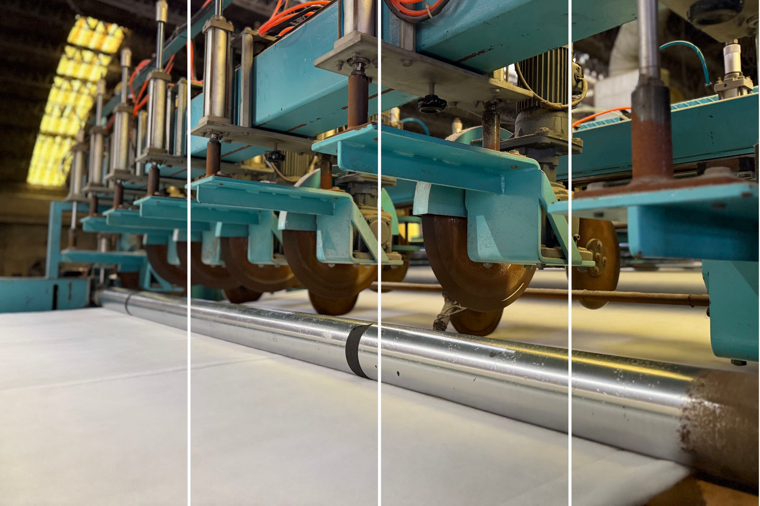 Close-up view of industrial machinery with blue metal components, pipes, and orange and black wires, set in an industrial or manufacturing environment.