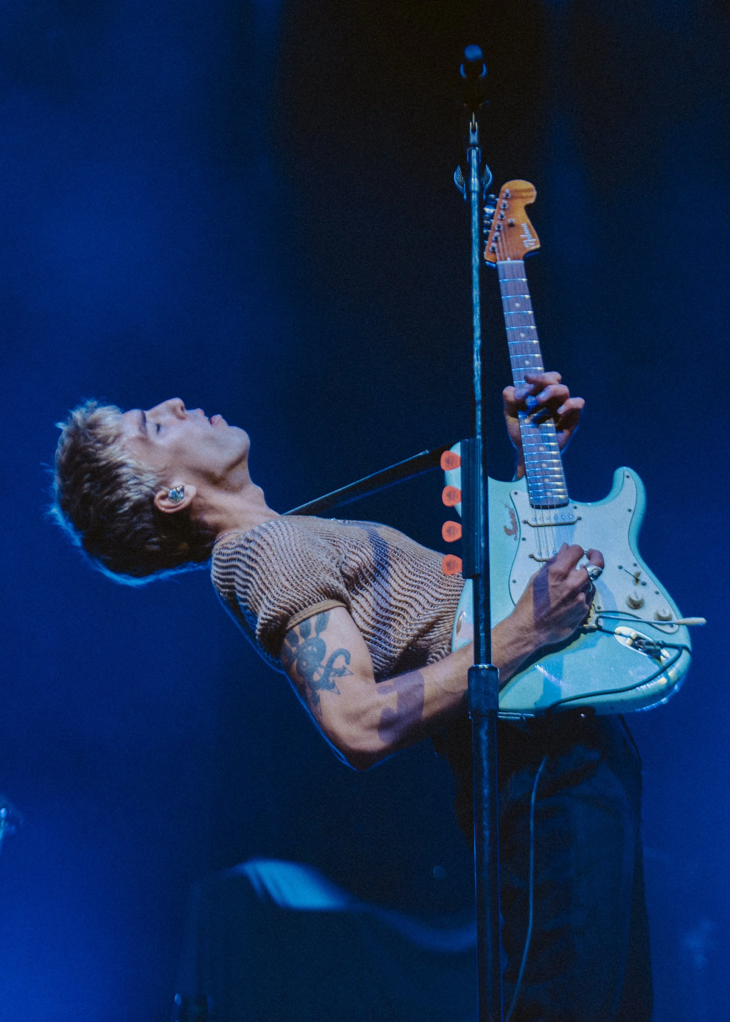Bad Suns playing an electric guitar on stage, illuminated by blue lighting.