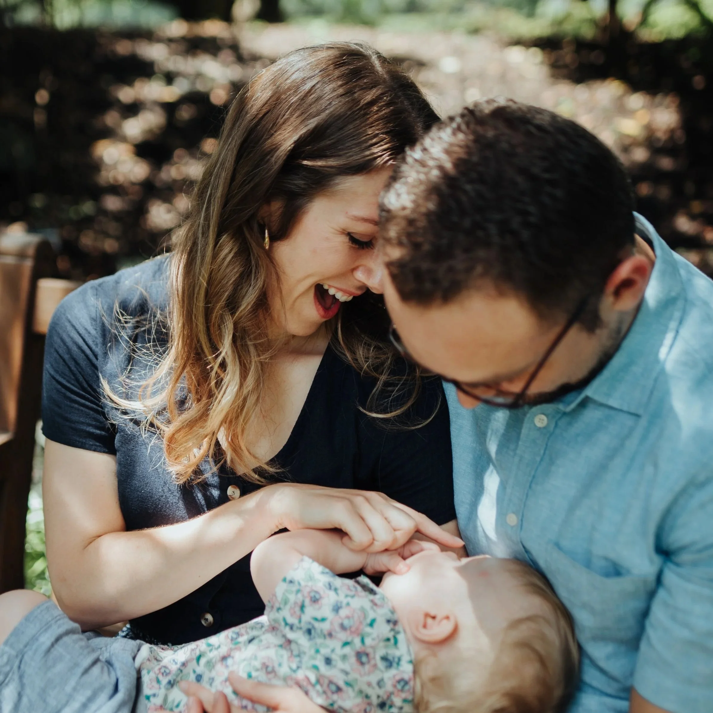 A young couple holding their baby smiling and touching foreheads outdoors.