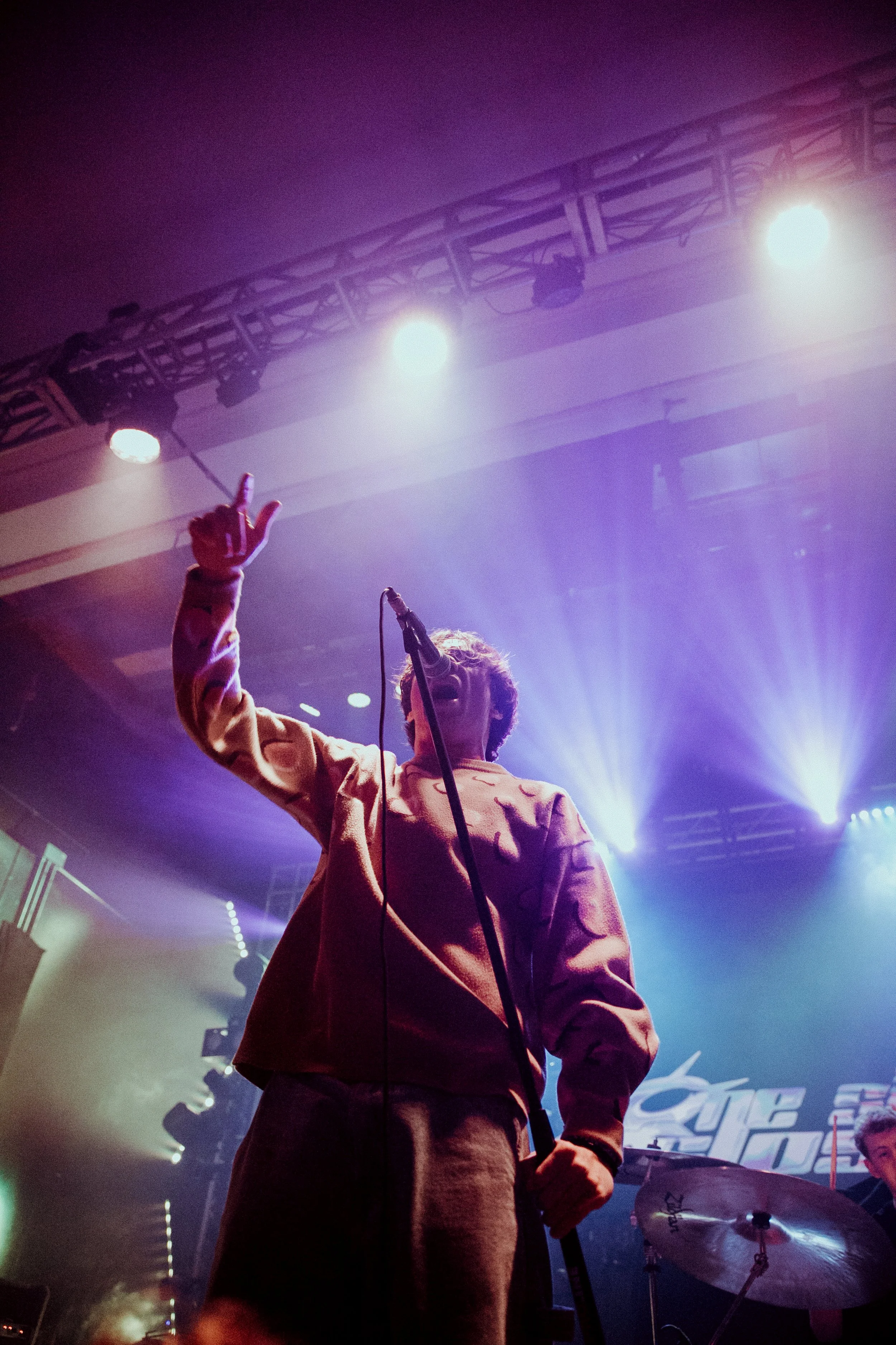 Arm's Length on stage with raised hand, colorful stage lights, and drum set in the background.