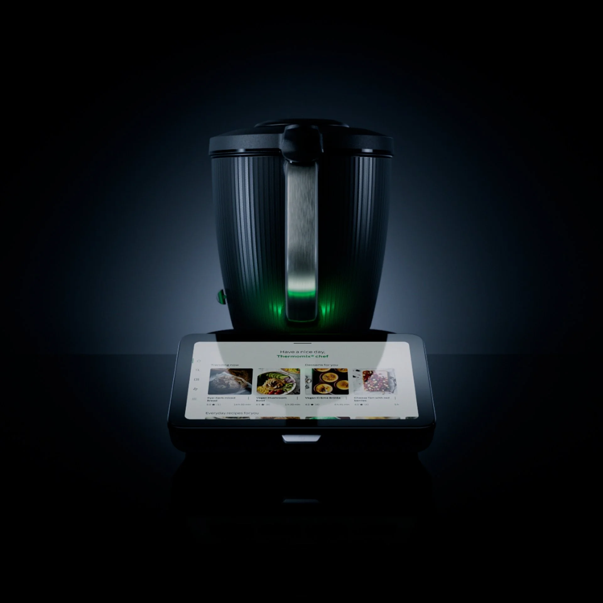 A smartphone displaying a recipe app with food images, placed under a black kitchen appliance, possibly a slow cooker or rice cooker, with a dark background.