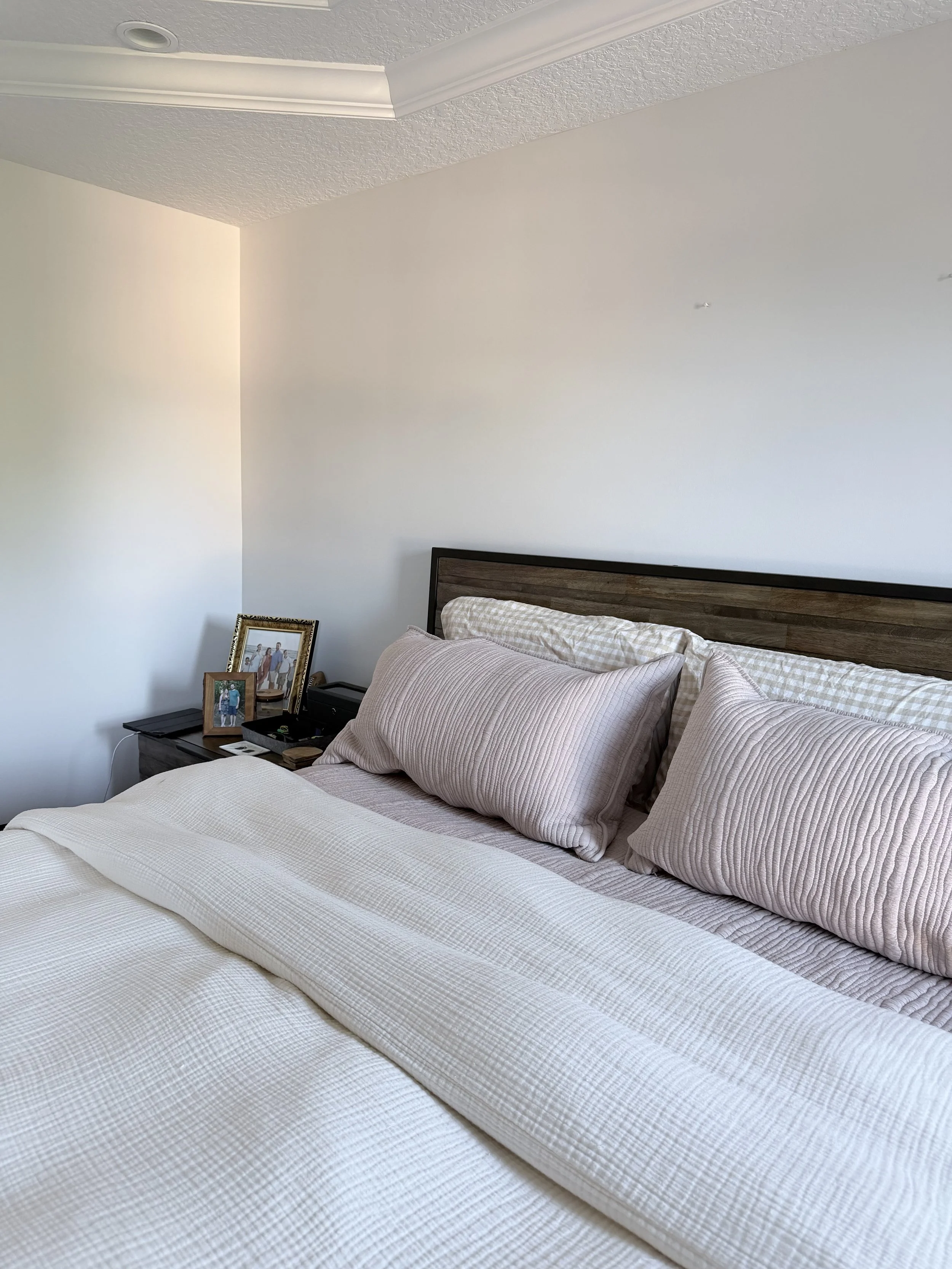 A bedroom with a bed, pillows, and a bedside table with family photos