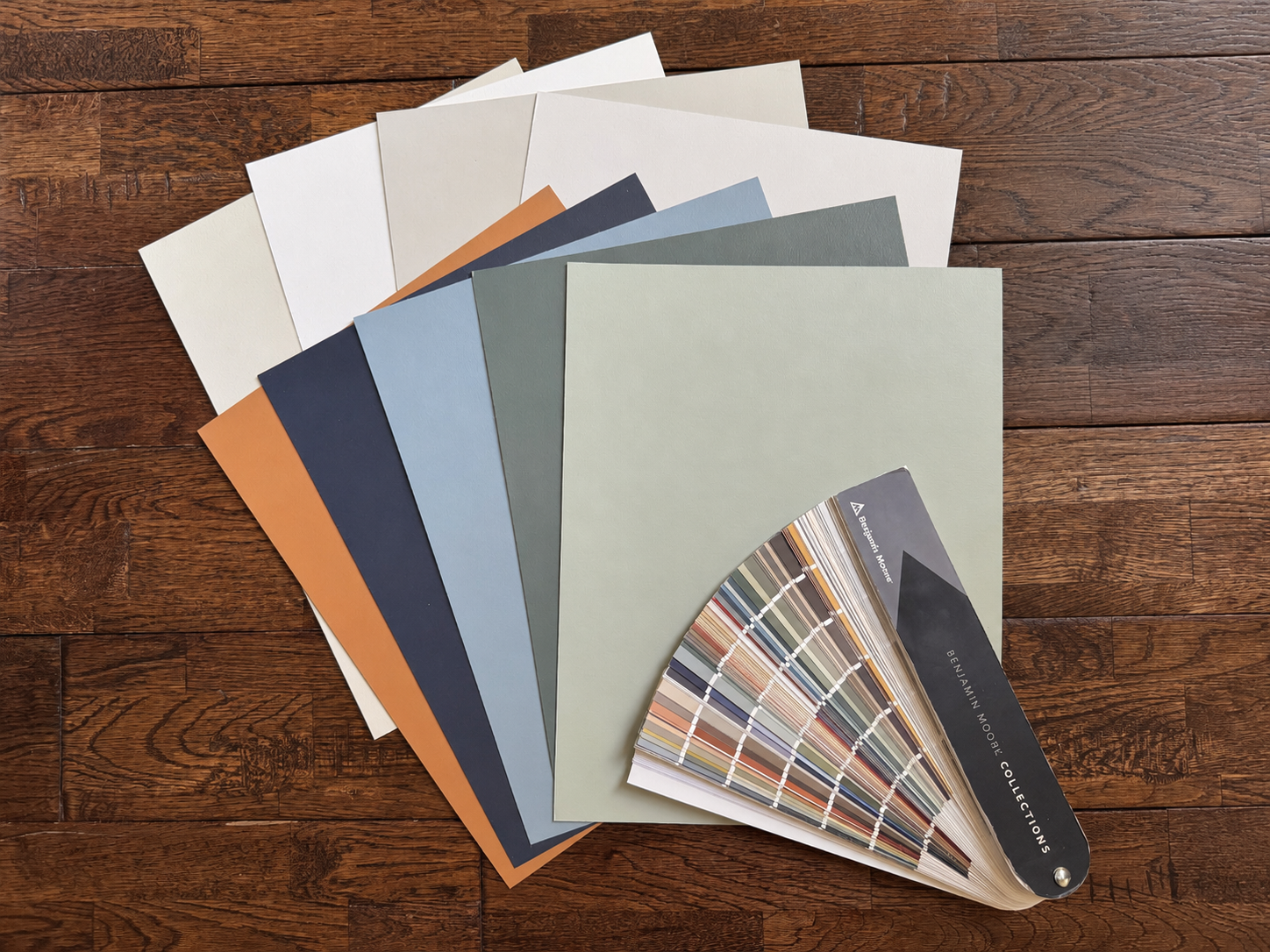 A color palette sample book with color swatches and paint color samples fanned out on a wooden surface.