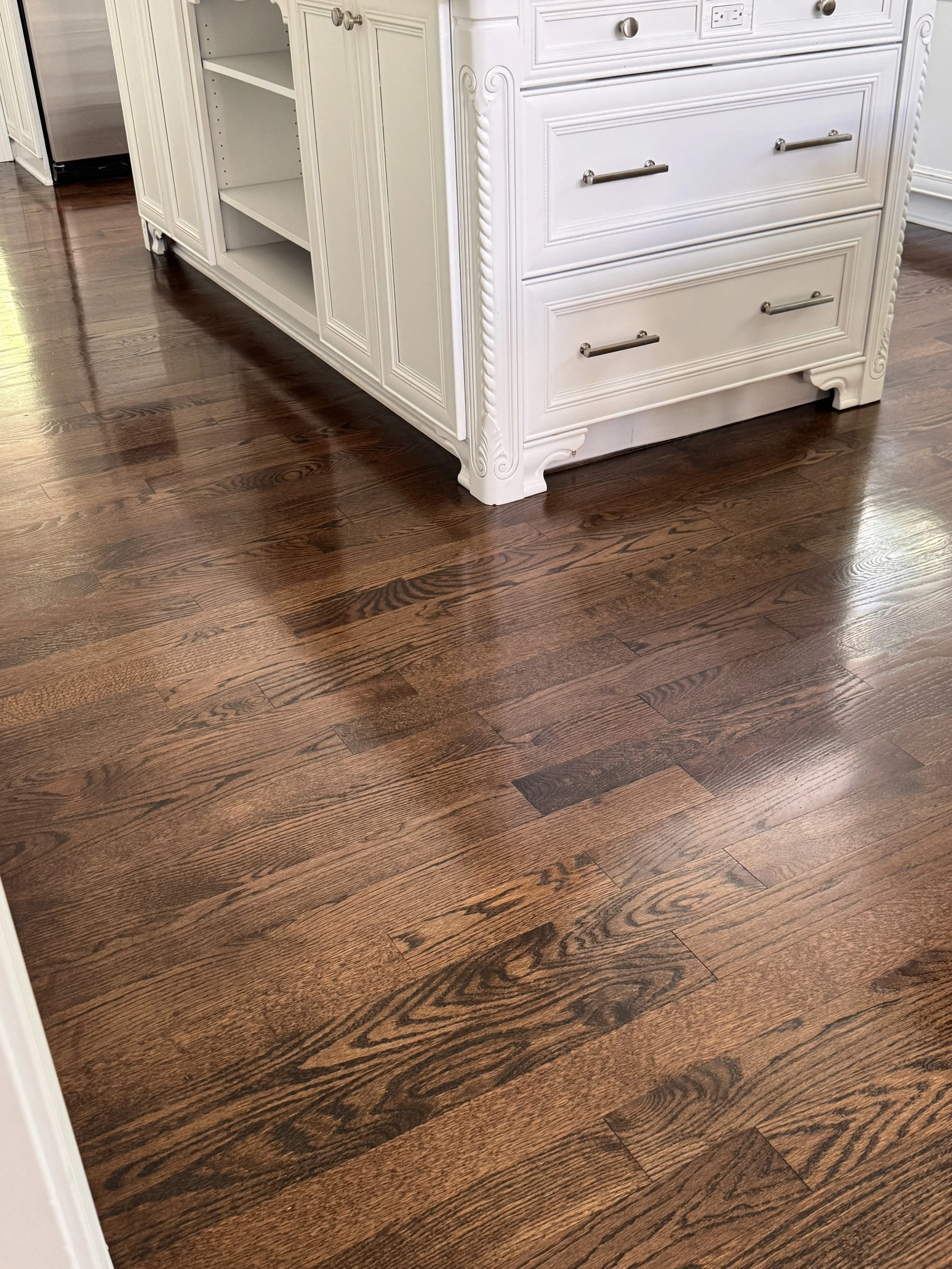 Close-up of a dark wooden floor in a room, with a white cabinet or dresser visible in the background.