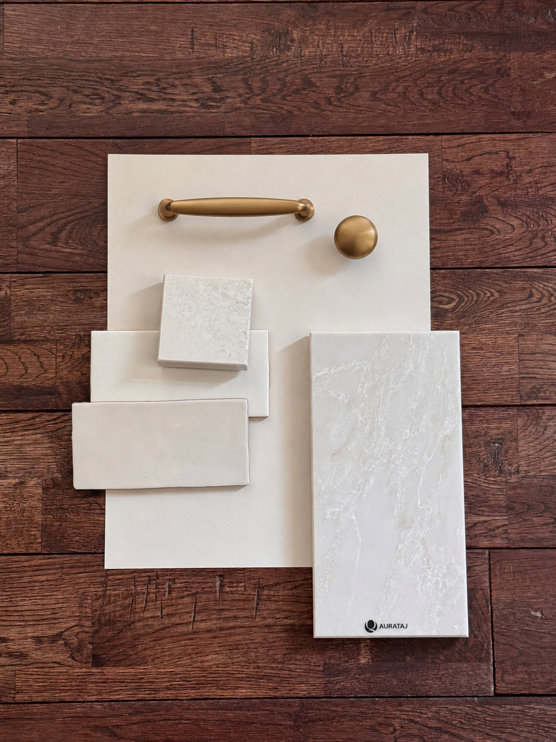 Arrangement of various tile samples and a brass door handle on a white backing board placed on a wooden floor.