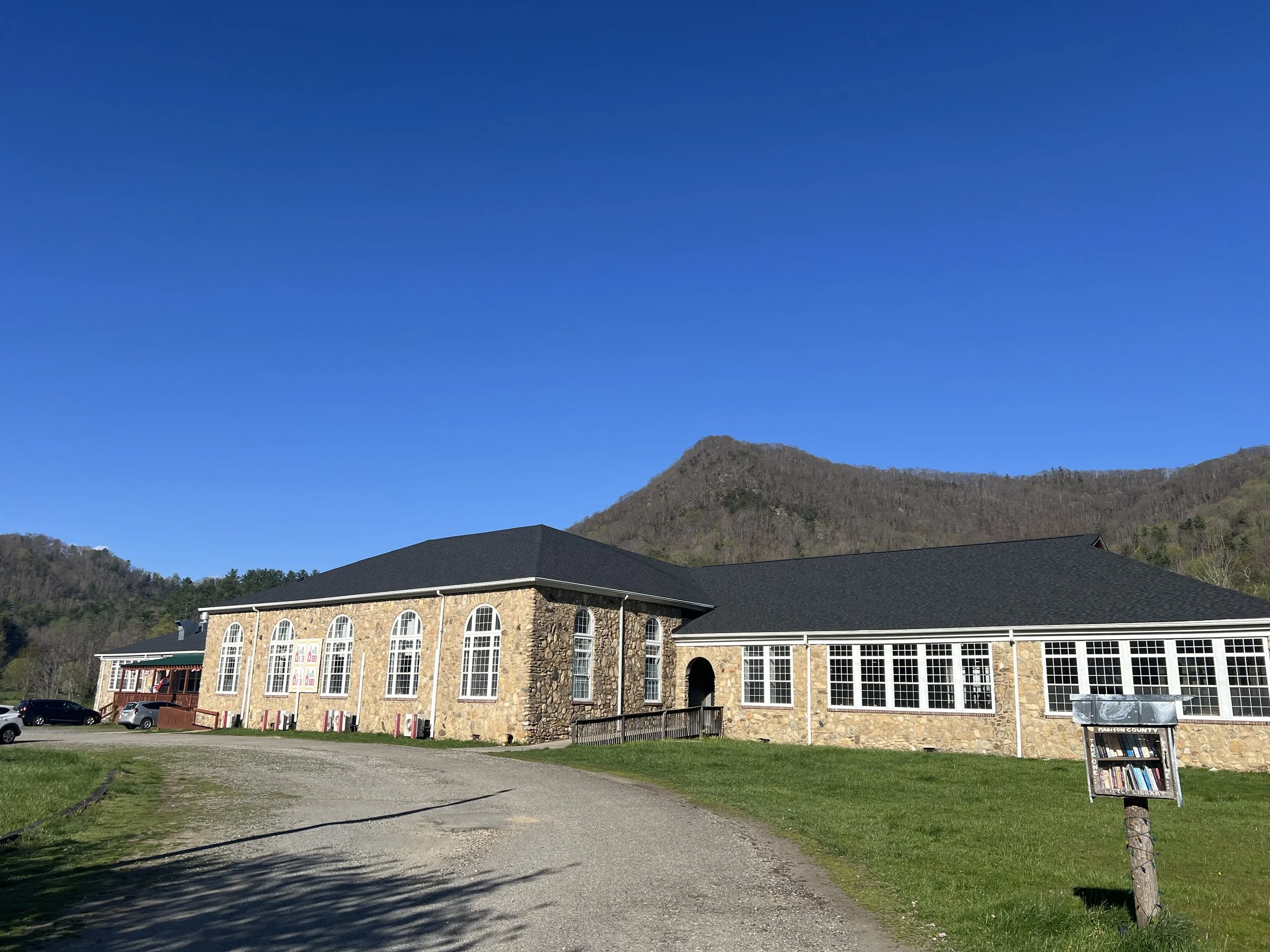 Building with large windows and stone facade against a mountain landscape under clear blue sky.