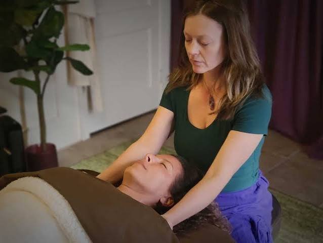 A woman receiving a massage from a massage therapist in a cozy, softly lit room.