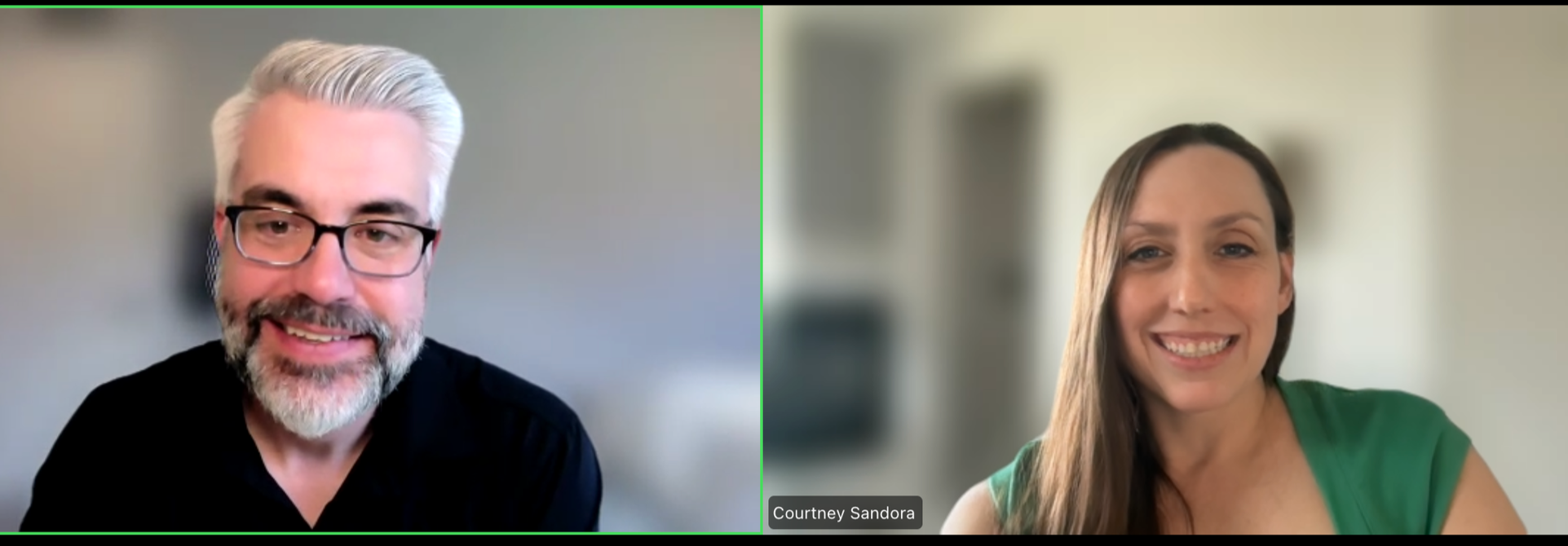 A man with gray hair, beard, and glasses wearing a black shirt on a video call with a woman with long brown hair and a green top, both smiling.