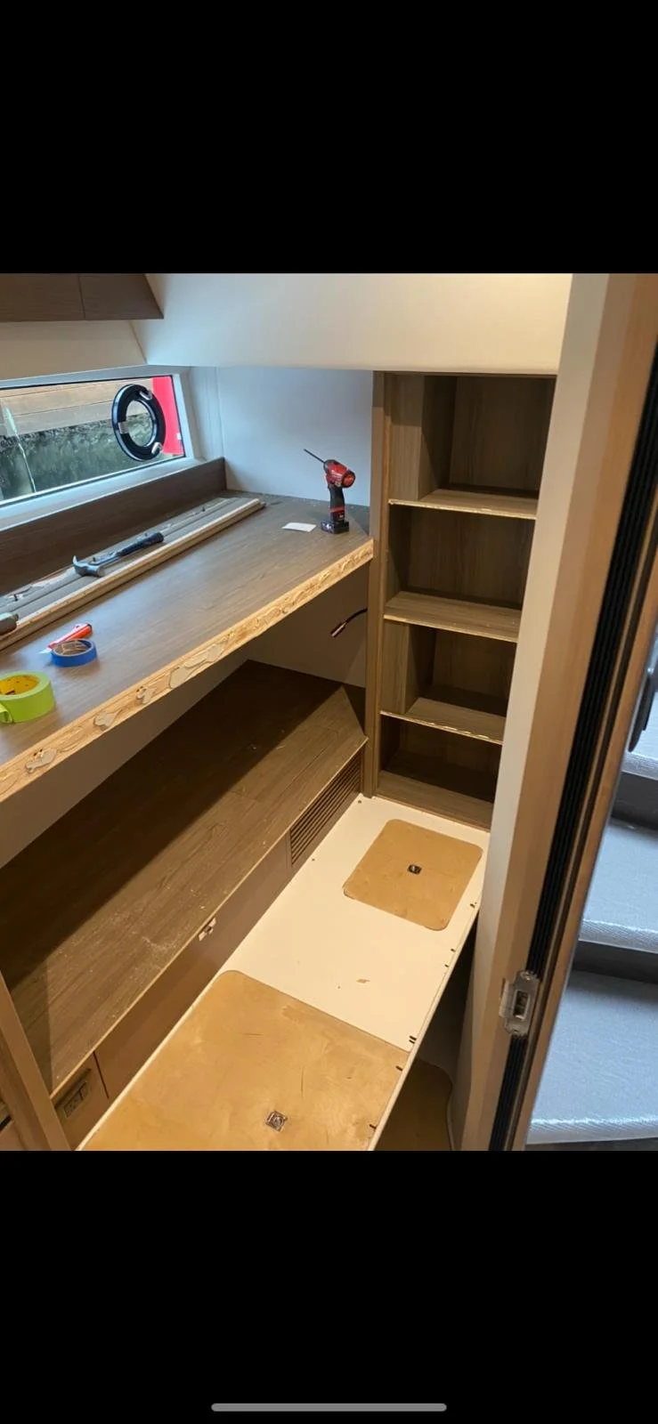 Wooden cabinet being assembled with a countertop, shelves, and a bottom drawer, inside a room with a window.