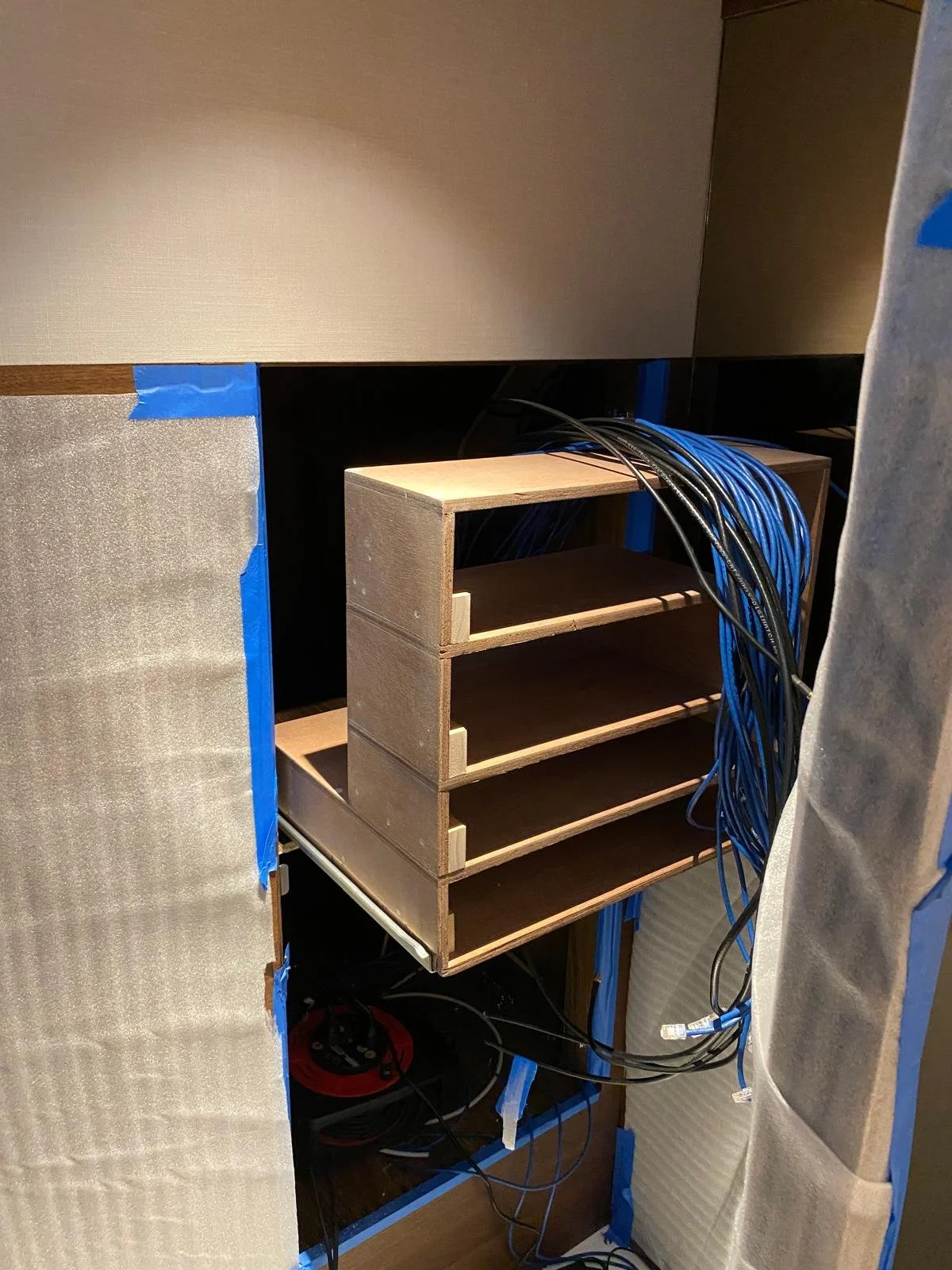Construction or wiring project with a wooden shelf and blue and black cables, partially covered with protective paper and tape.