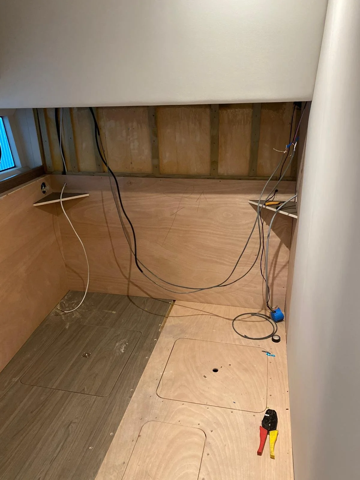 Partially constructed wall with electrical wiring and access panels on the floor, indicating ongoing renovation or electrical work.
