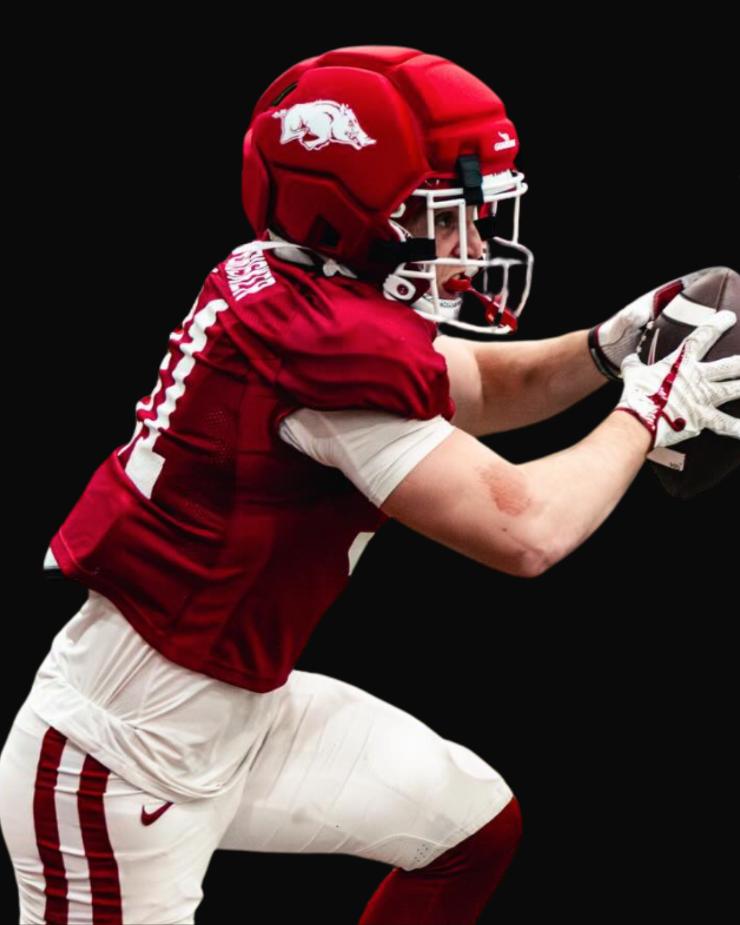 A football player in red and white uniform catching a football, wearing a red helmet with a white logo, against a black background.