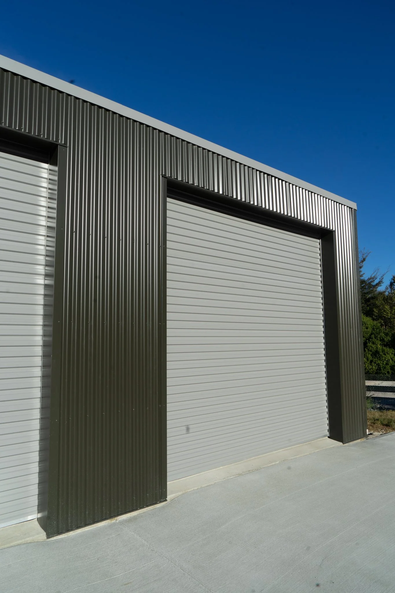 Image of a metal building with roll-up doors, gray and black exterior, under a clear blue sky.