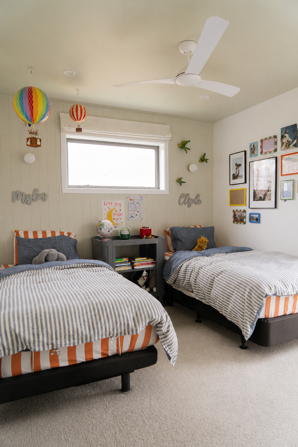 A children's bedroom with two beds, colorful decorations, framed photos, and a ceiling fan.