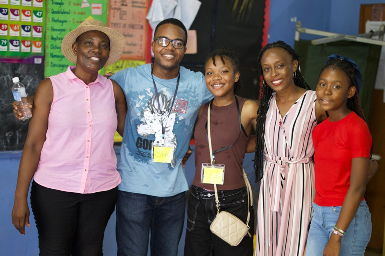 Group of five people, including women and children, standing together in a classroom, smiling for the photo.