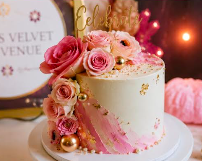 A decorated birthday cake with pink roses, gold accents, and a gold 'Celebration' topper.