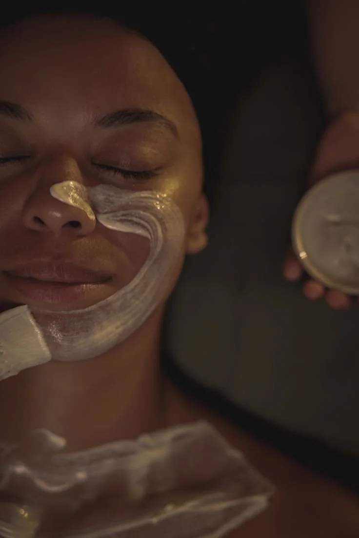 Person receiving a facial treatment with cream applied to their face while lying down with eyes closed.