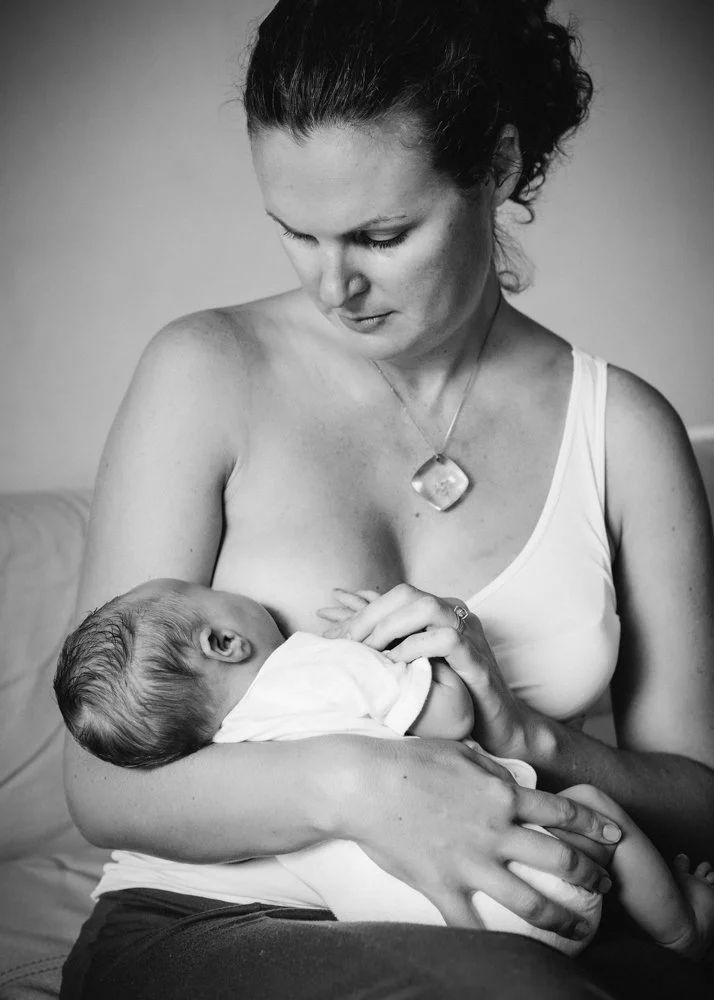 A woman breastfeeding a baby while sitting on a couch, in black and white.