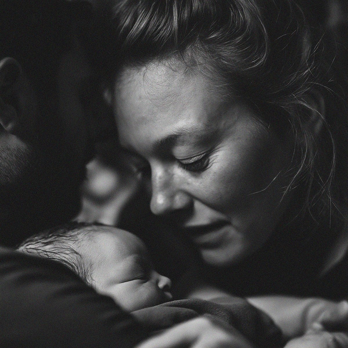 A black and white close-up photograph of a woman and a baby, with their foreheads touching in a tender, intimate moment.