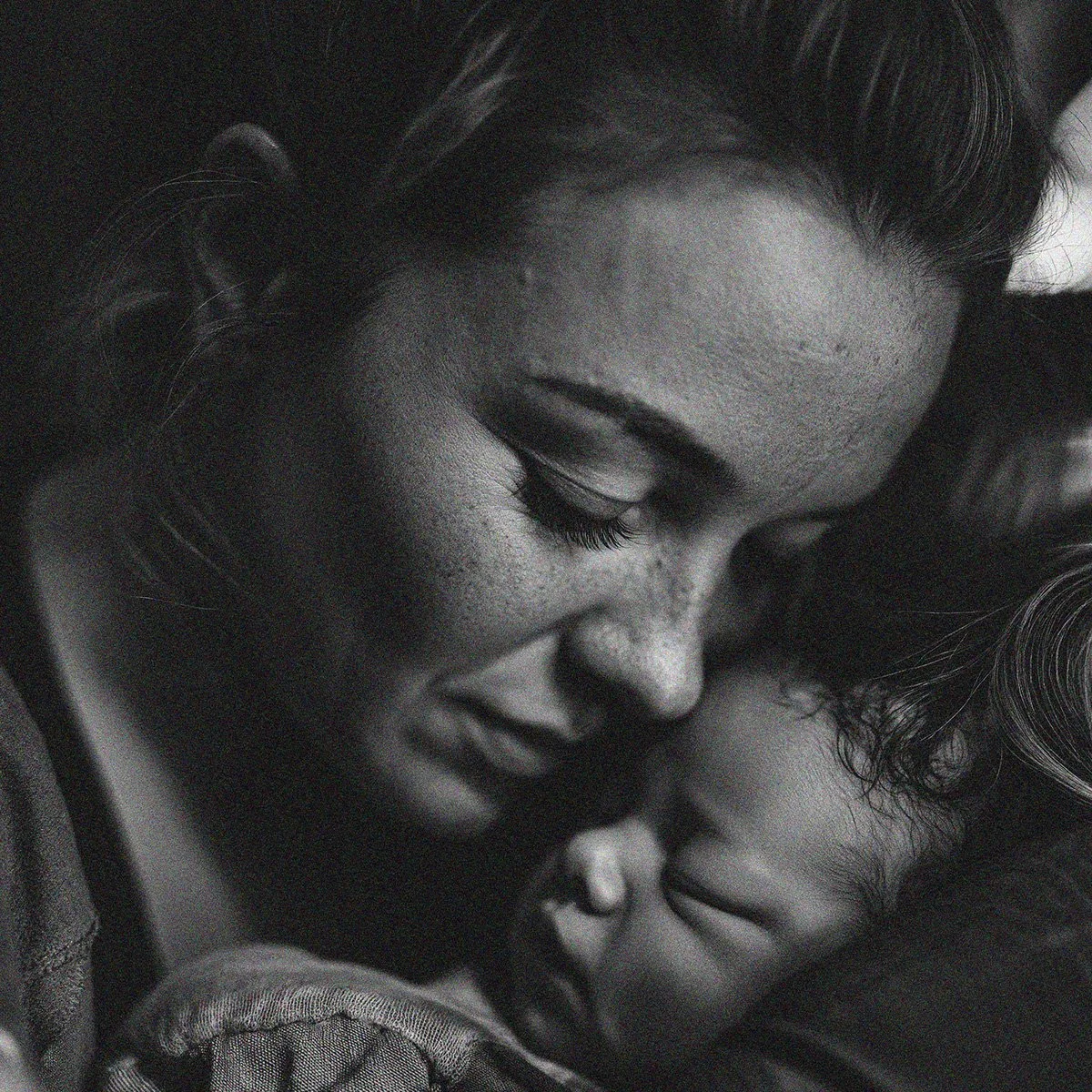 A black and white close-up photo of two women in an embrace, smiling with their eyes closed, showing a moment of affection and closeness.