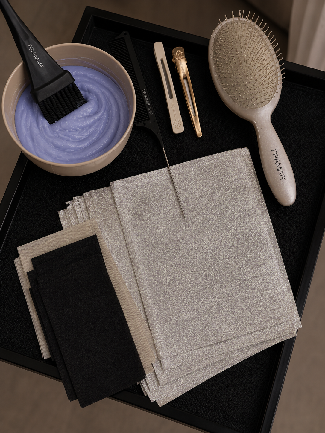 Hair dye, hairbrush, cotton swabs, hair clips, hairbrush, and paper towels on a black surface
