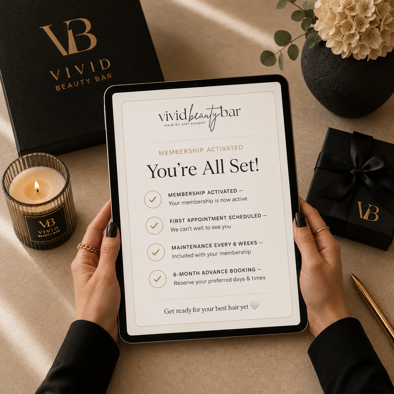 A person holding a tablet displaying a membership activation confirmation for Vivid Beauty Bar, with a gift box, a candle, and a vase with flowers in the background.