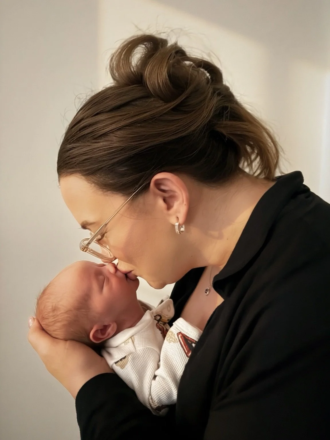 A woman with glasses holding a newborn baby close to her face.