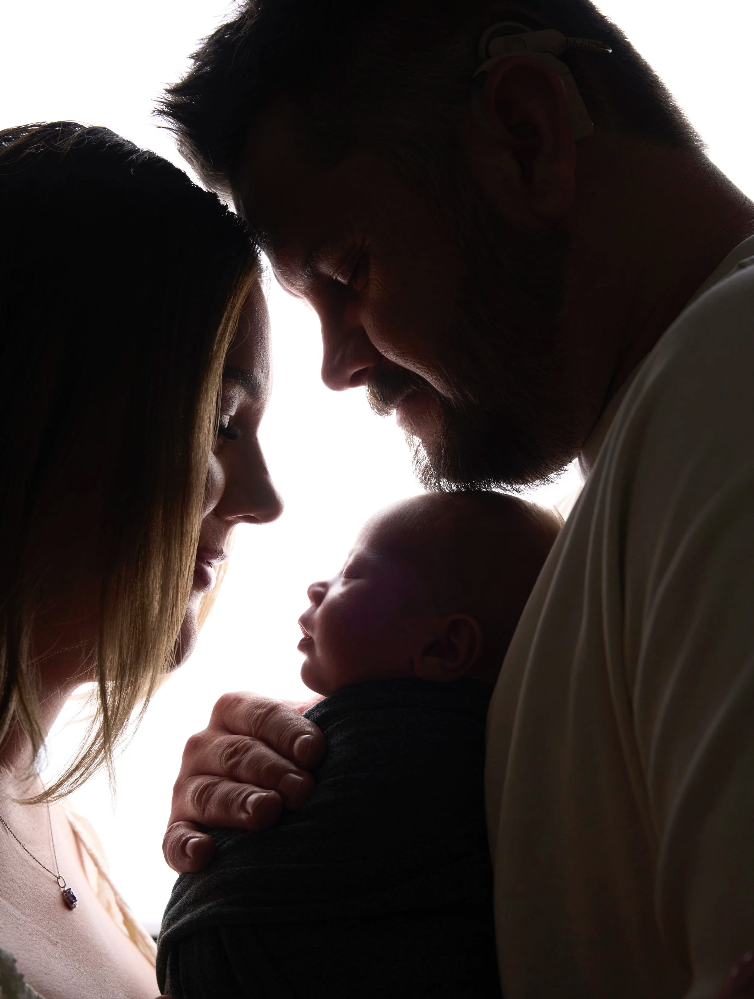 Silhouette of a father and mother touching foreheads with their baby, creating an intimate moment of love and connection.