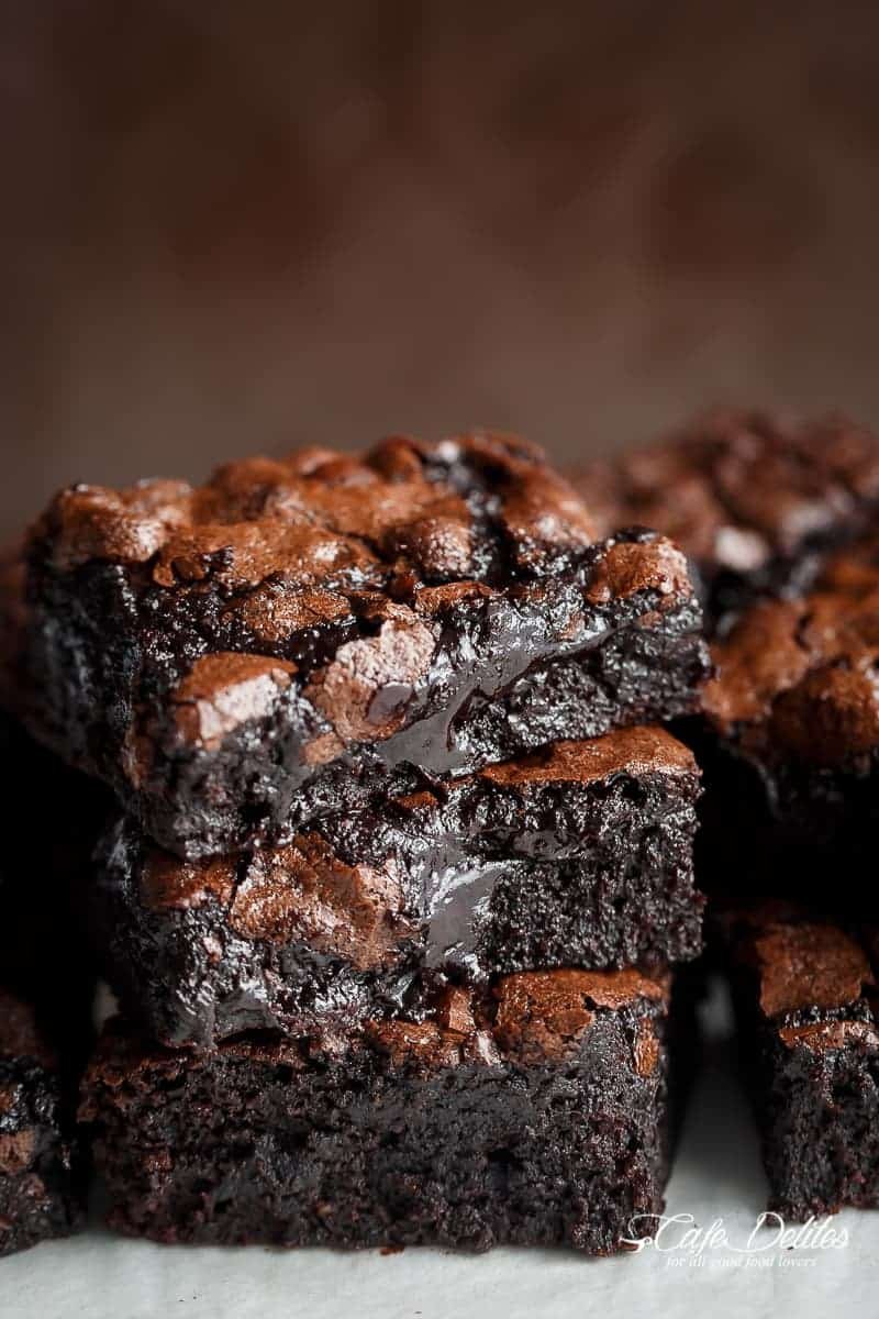 Close-up of three stacked double chocolate brownies with a gooey, melted chocolate center, on a white surface.