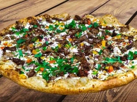 A large pizza topped with chocolate, green sprinkles, and colorful candy pieces on a wooden table.