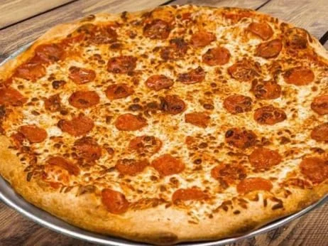 Large pepperoni pizza on a metal tray on a wooden table.
