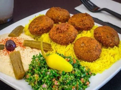 Plate of six falafel balls with yellow rice, pickles, and tabbouleh salad.